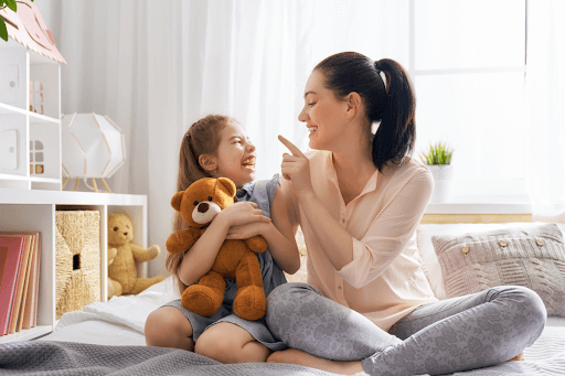 Mum, child and a teddy bear on a bed, engaging in play