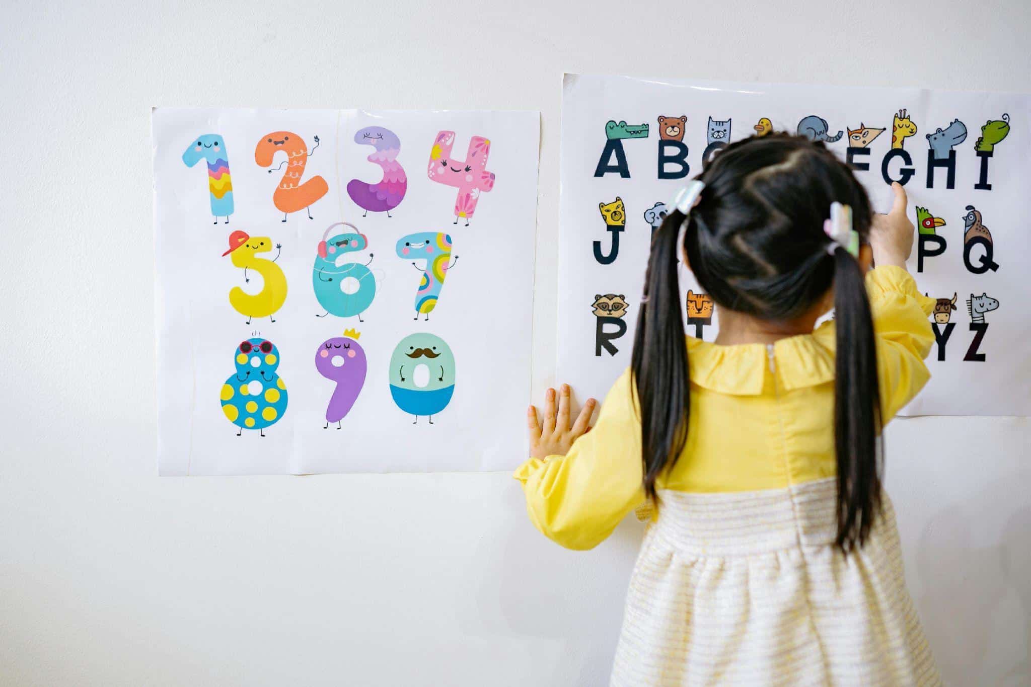 A young girl pointing at an ABC poster, demonstrating early literacy skills for preschoolers