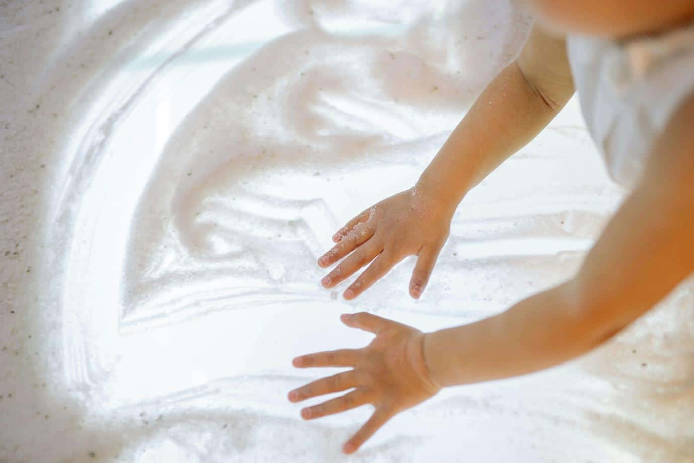 A baby's hands playing with white sand on a lightbox, demonstrating an example of a baby sensory development activity