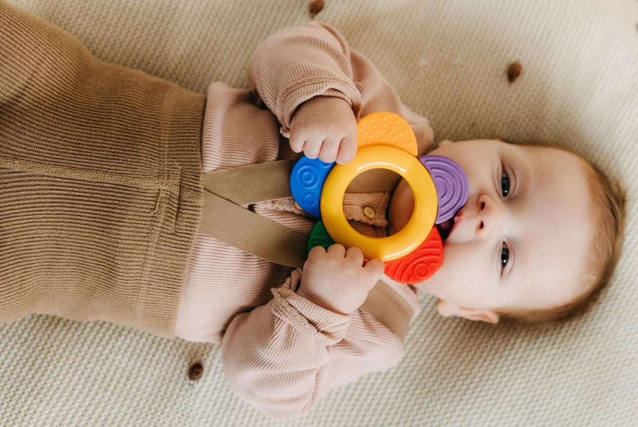 A baby holding a colourful chew toy often used for five senses in infant development for baby development