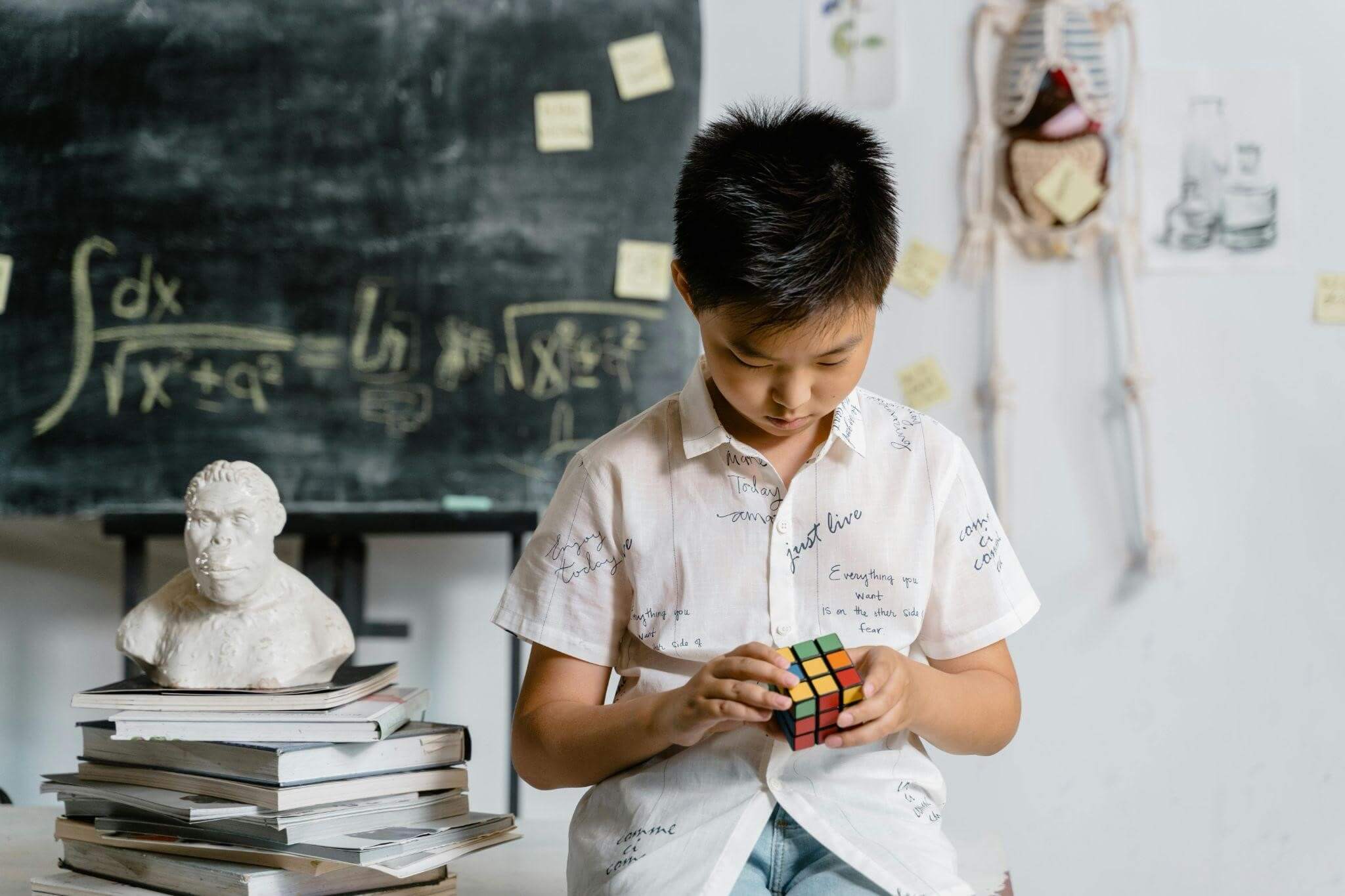 A boy is holding a Rubik's cube in a classroom environment, he seems to be attempting to solve it.