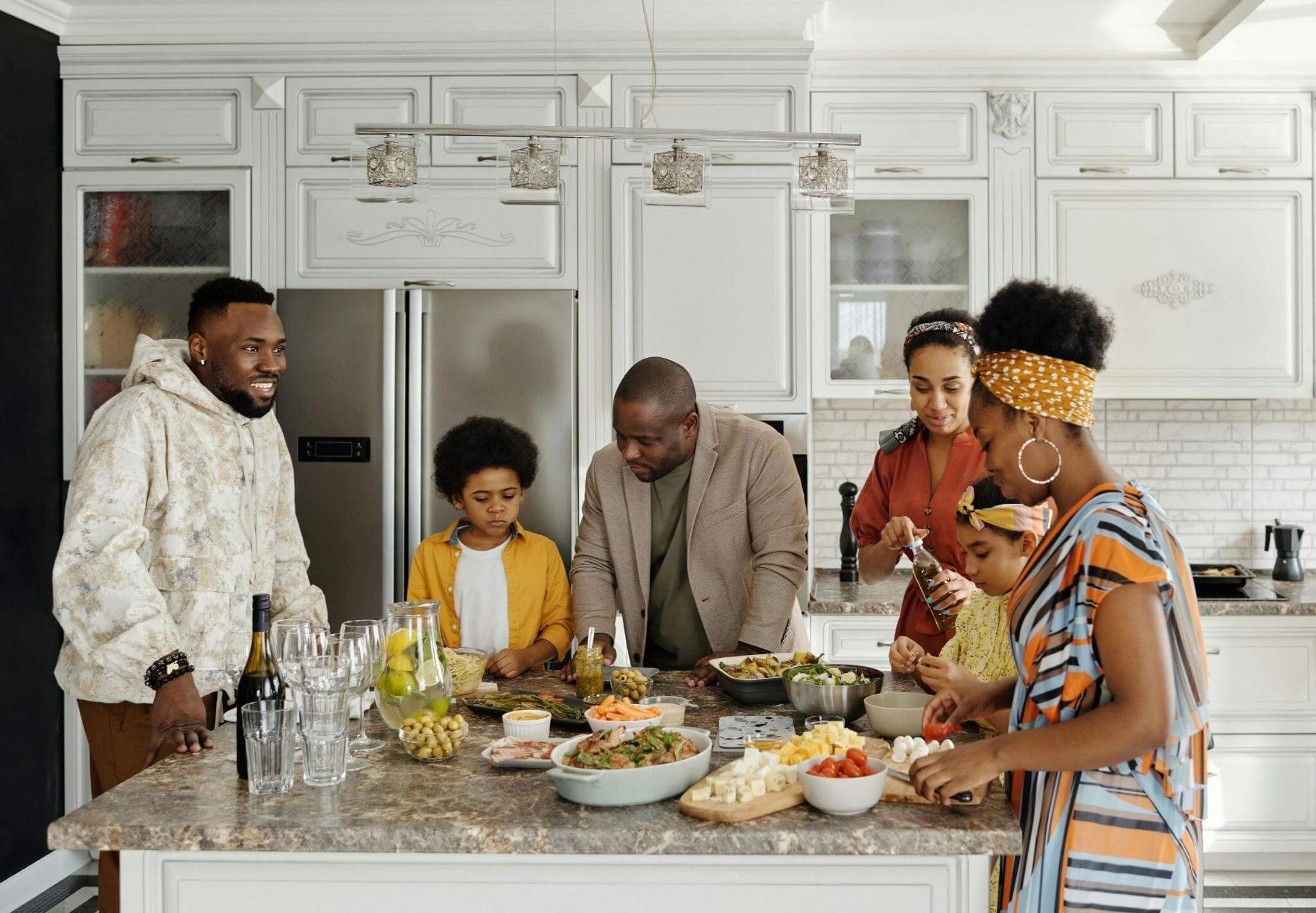 A Family in a kitchen gathering for meal time, there are four adults and two children