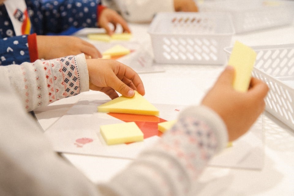 A preschooler is solving a 3D puzzle tangram challenge during a Shichida class