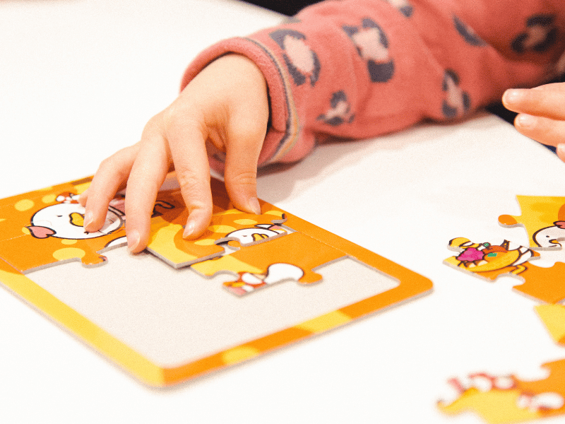 Benefits of puzzles for toddlers, featuring a toddlers hand building a puzzle on a table.