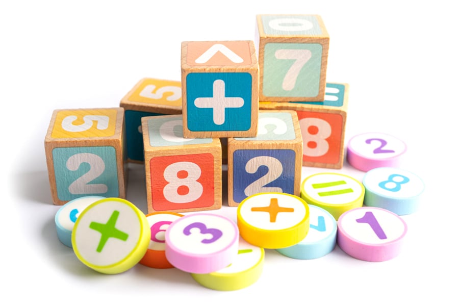 Maths games for kids, featuring a pile of stacked wooden blocks and plastic round chips, featuring mathematical symbols and numbers on each.