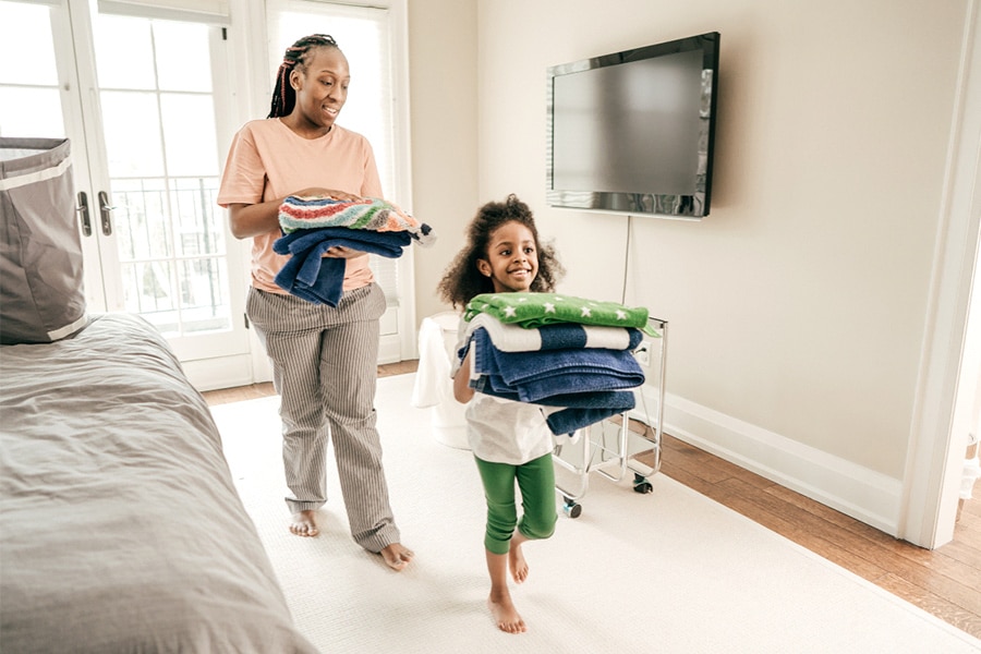 A mum and preschooler are packing away folded laundry together.