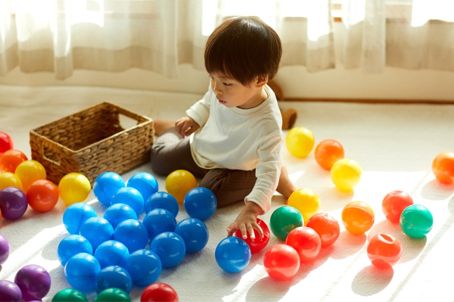 A toddler is sorting a variety of plastic, coloured balls.
