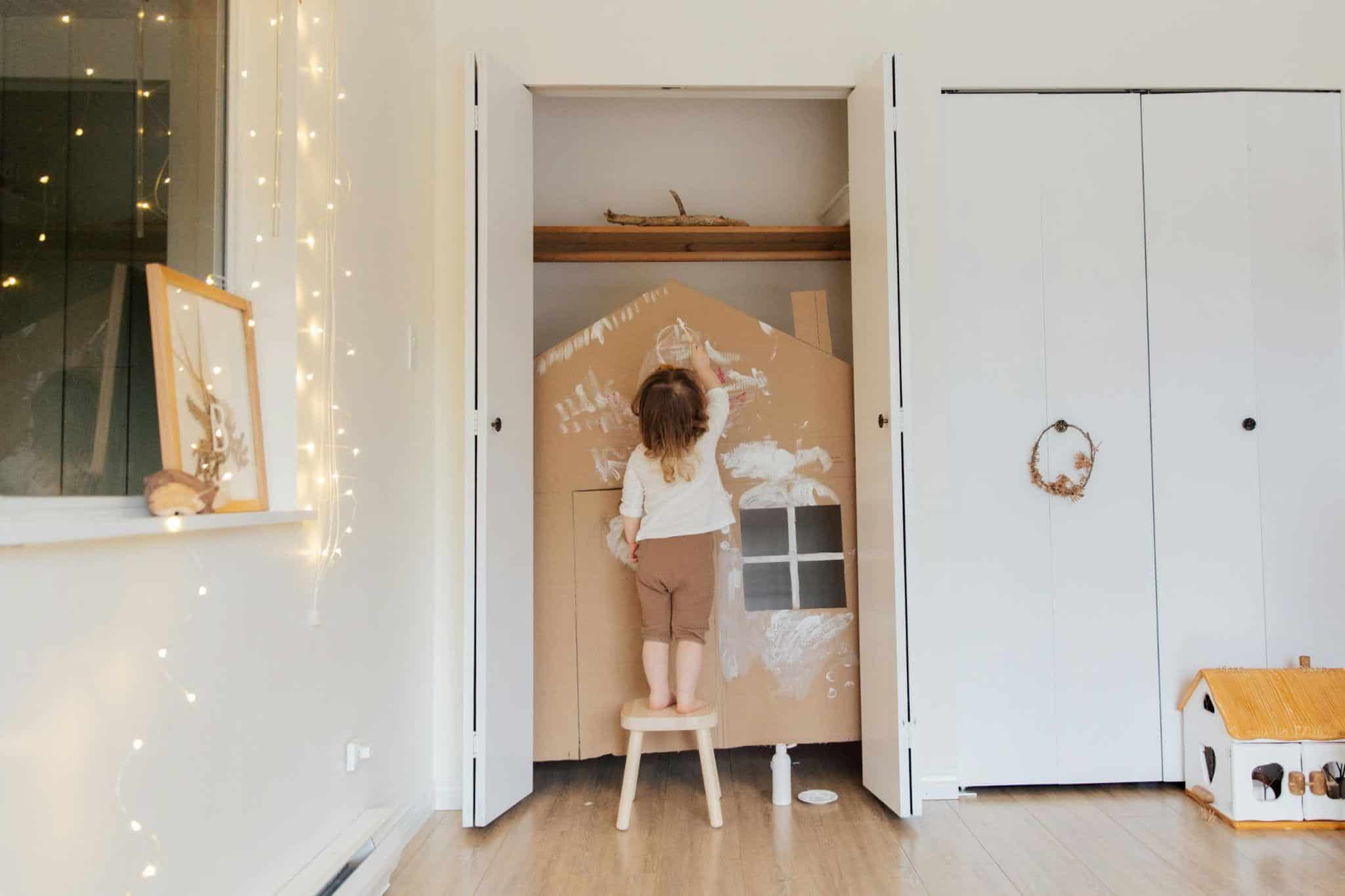 a child standing on a stool in a room with a cardboard house