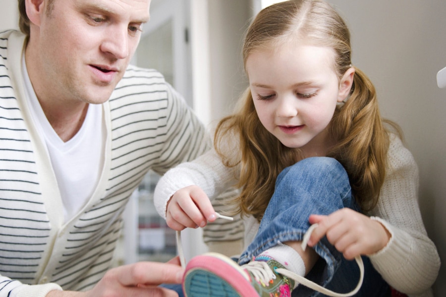Goal setting for kids, here a preschooler is tying her shoelaces, while her dad encourages her.