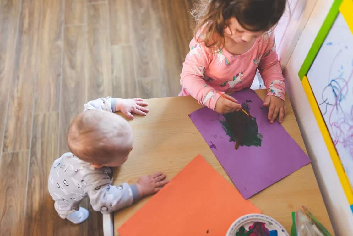 A child is seen painting and drawing at a table, she is very focused on her art