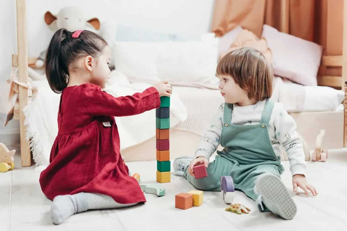 Fine motor activities for toddlers. Two toddlers playing with wooden blocks, practicing their fine motor skills through play.