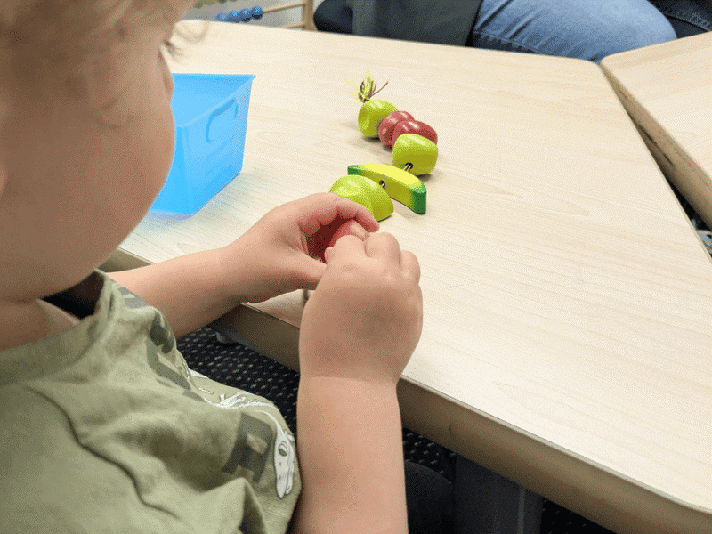 A toddler completing a stringing activity. Threading activities build concentration and fine motor control while engaging the senses through touch, vision and movement.