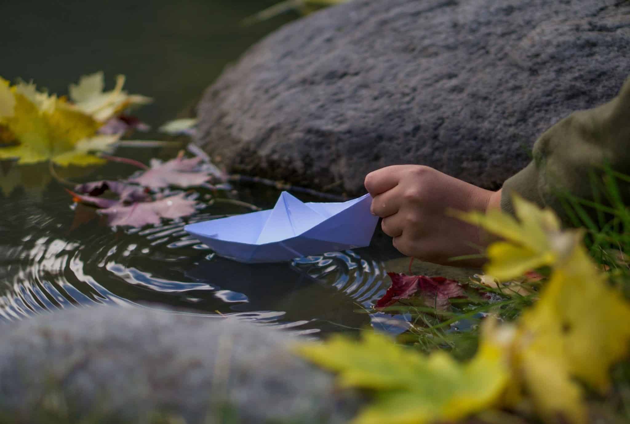 A person gently holds a paper boat afloat in calm water, showcasing a moment of creativity and tranquility