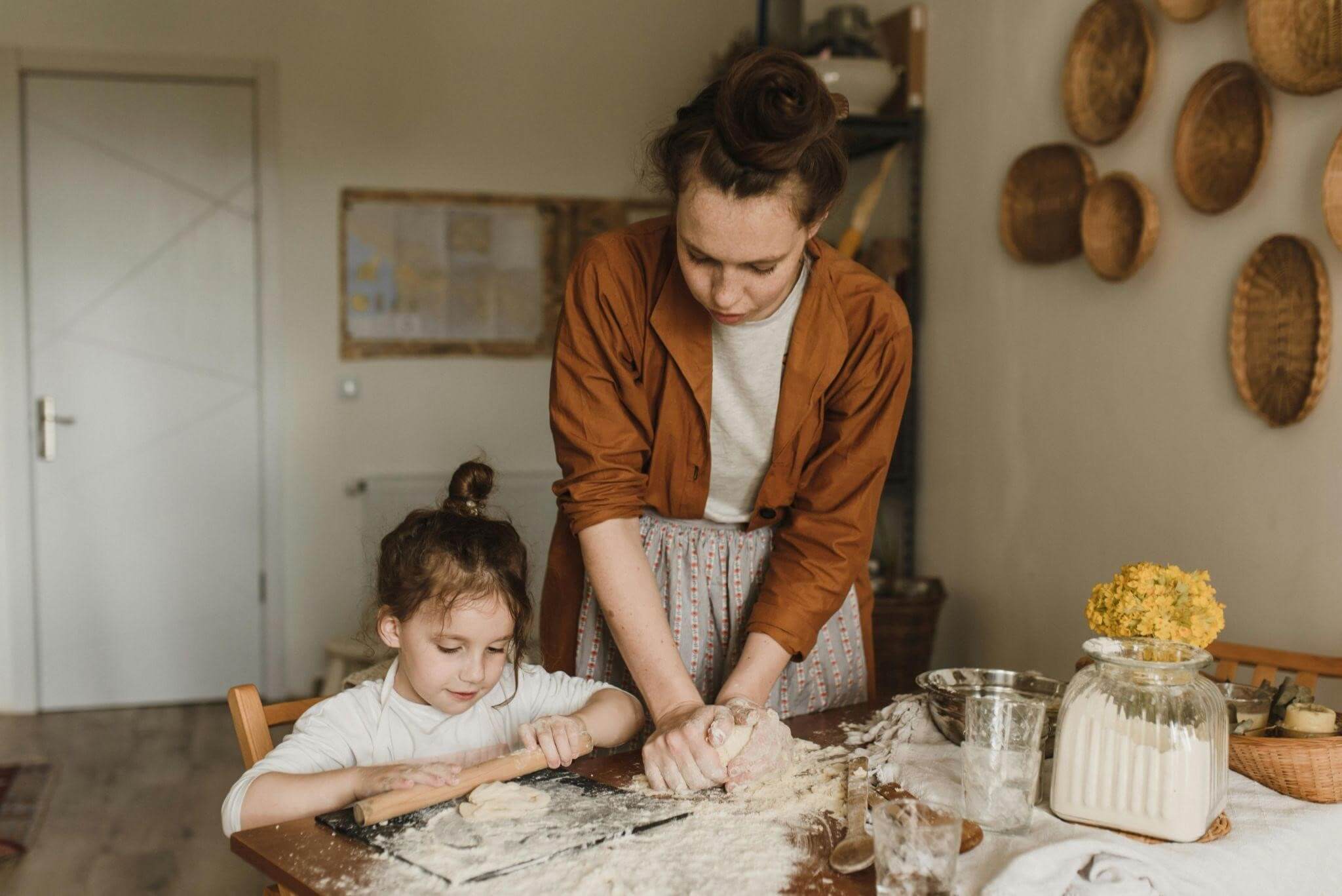 A woman and a child are joyfully making pasta together in a bright kitchen, surrounded by ingredients and utensils