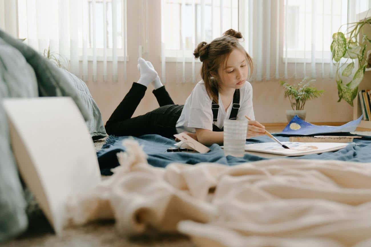 Fun activities for kids - Kid in White shirt painting while lying on her stomach, painting.