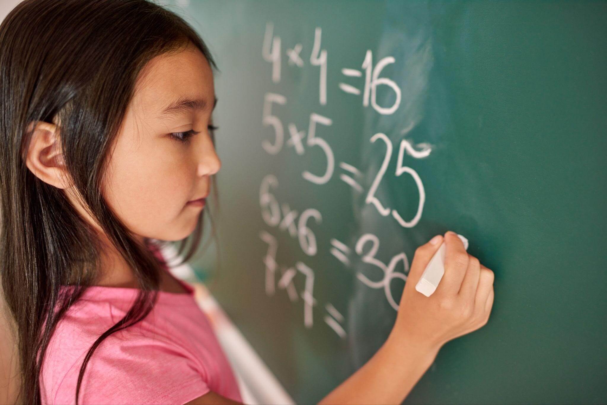 A young girl writing with chalk on a blackboard, focused and engaged in her task